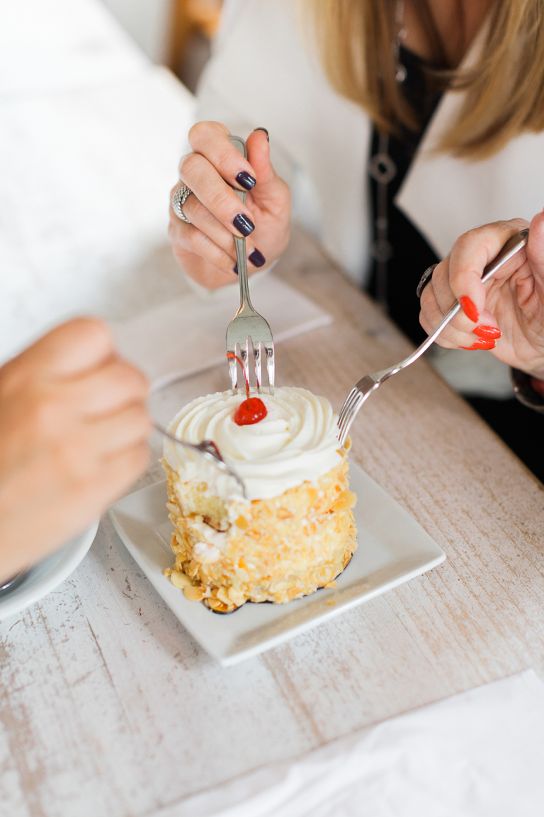 three friends hands with forks sharing one delicious dessert cake with cream and cherry on top